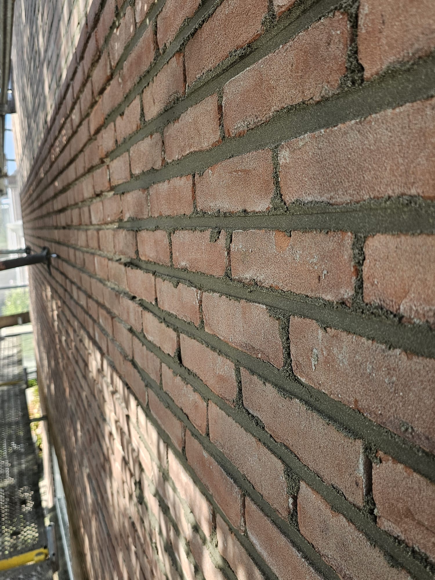 Close-up van rode bakstenen gevel met vernieuwd voegwerk in lange zijmuur Uithakken van bestaand voegwerk in bakstenen gevel