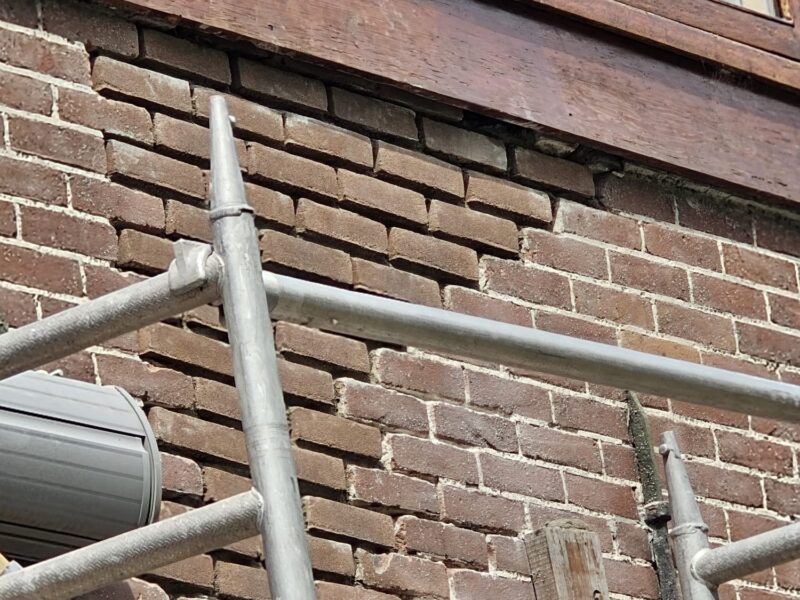 Gevelrenovatie onder houten kozijnen met steigerwerk bij oudere woning Lateiherstel en constructief gevelherstel aan onderzijde van bakstenen muur