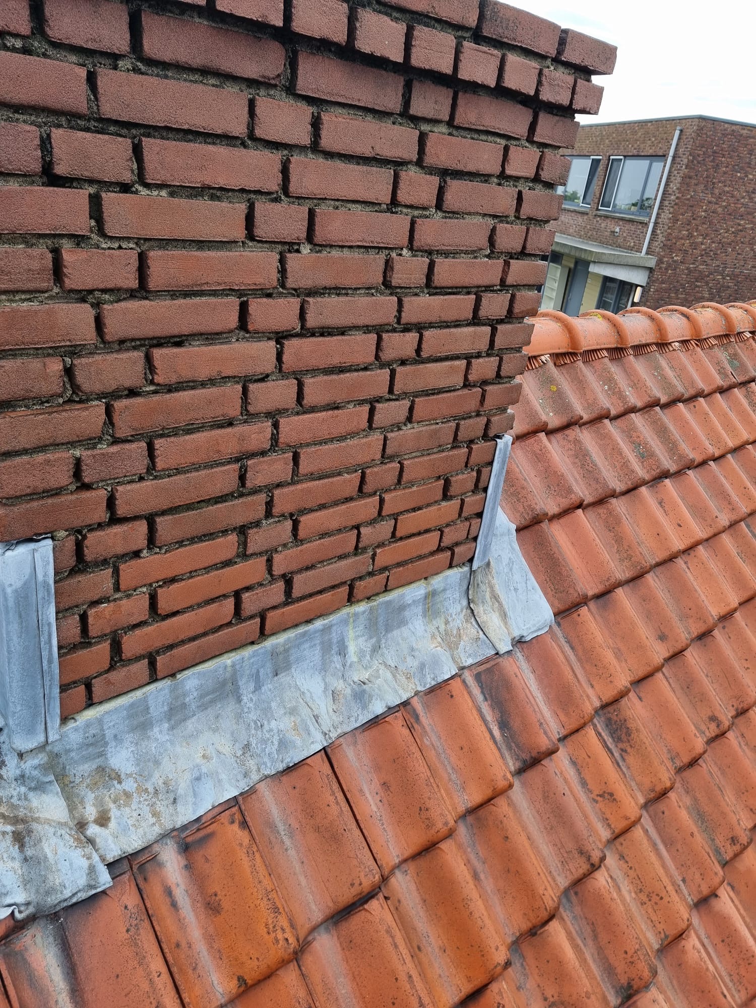 Beschadigd voegwerk aan bakstenen schoorsteen op hoogte