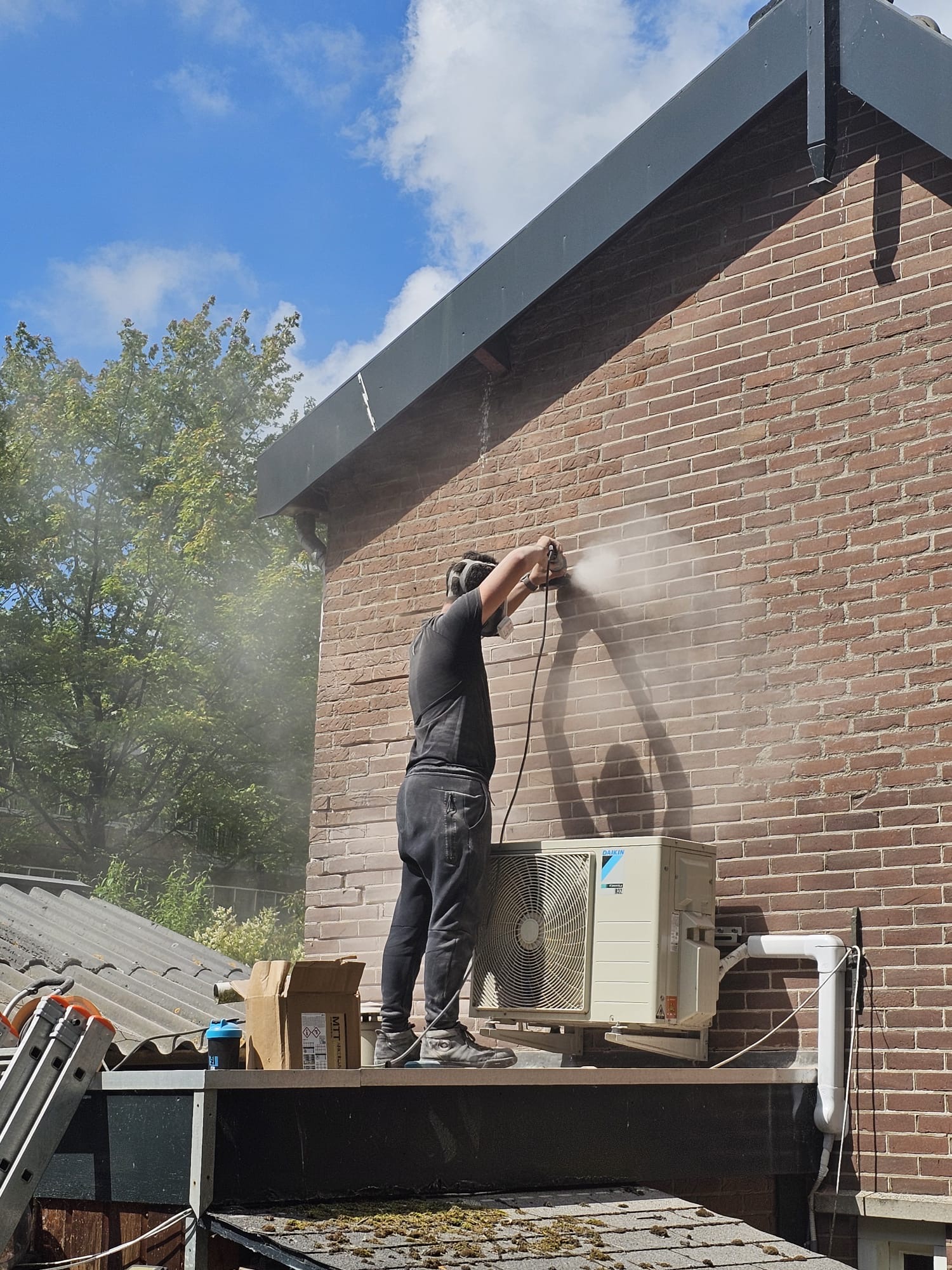 Vakman reinigt bakstenen buitenmuur met hogedrukreiniger en waternevel Gevelreiniging als voorbereiding op gevel impregneren