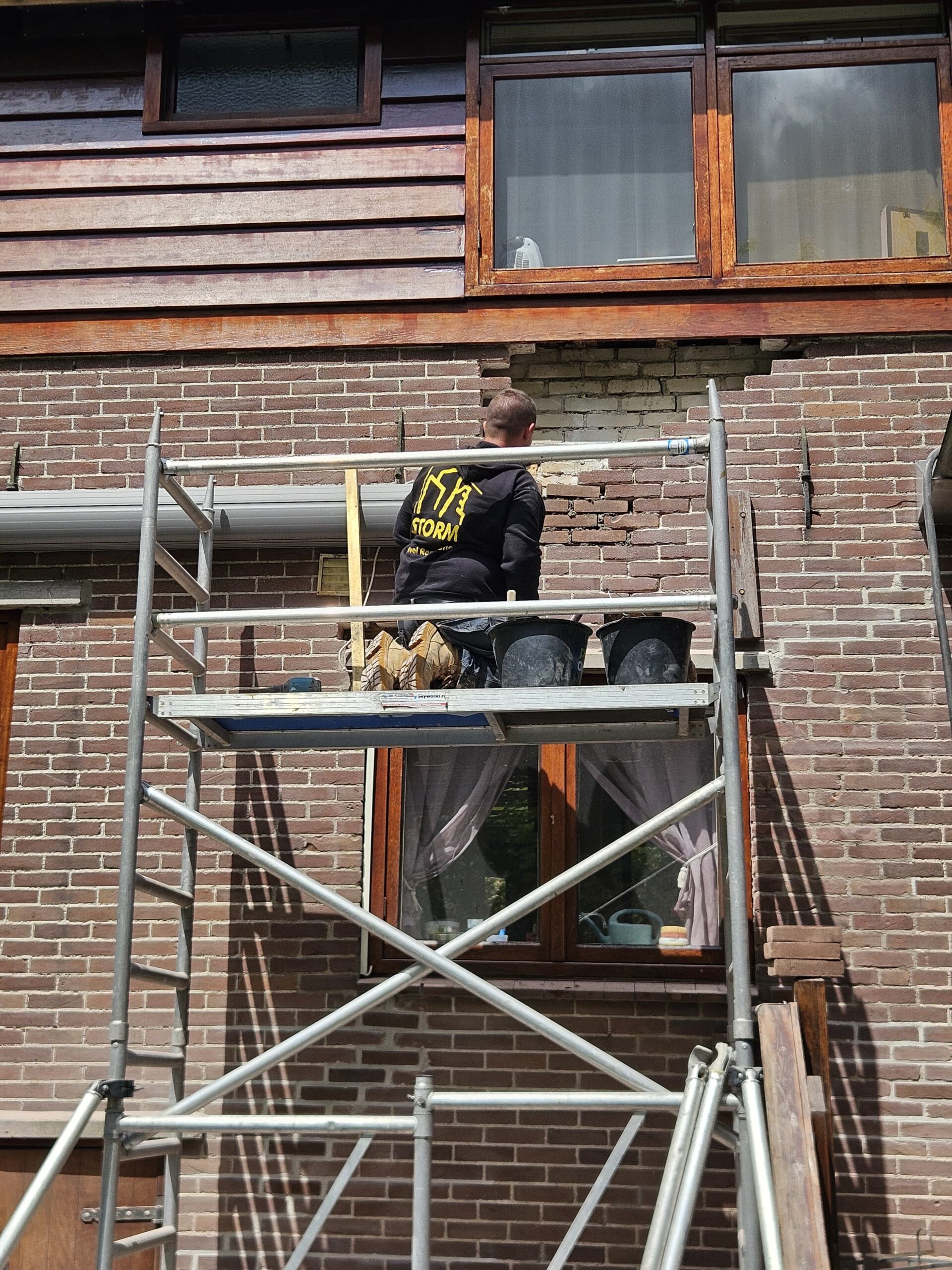 Vakman renoveert gevel van oudere woning vanaf steigerconstructie Vakman renoveert gevel van oudere woning vanaf steigerconstructie