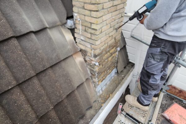 Vakman voert schoorsteenreparatie uit naast dakpannen