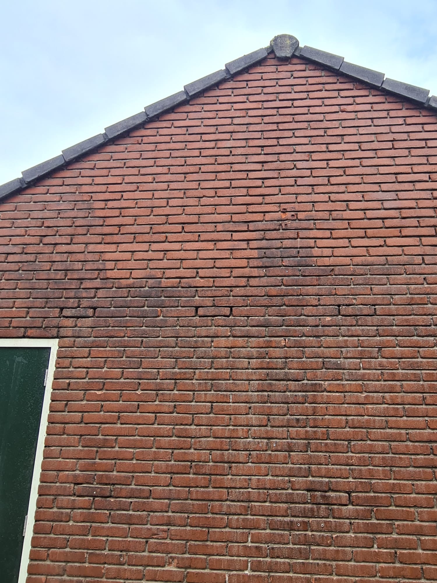 Verouderde rode bakstenen kopgevel met zichtbaar voegwerk en dakrandafwerking Poreuze bakstenen gevel met verweerd voegwerk klaar voor impregneren